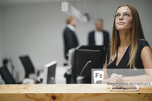 Businesswoman standing in office  leaning on wooden counter  looking up