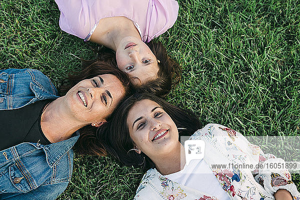 Lächelnde Mutter mit Töchtern auf einer Wiese im Park liegend