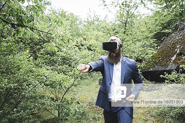 Businessman practicing martial arts while looking through virtual reality simulator against trees in forest