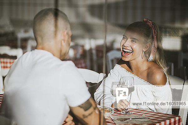 Glückliche Frau  die ein Weinglas hält und ihren Freund in einem Restaurant durch ein Fenster betrachtet