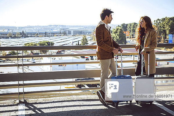 Business couple talking while standing on elevated walkway at airport