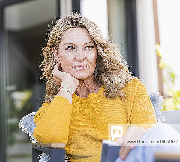 Porträt einer nachdenklichen reifen Frau  die mit einem digitalen Tablet auf einer Terrasse sitzt und in die Ferne schaut