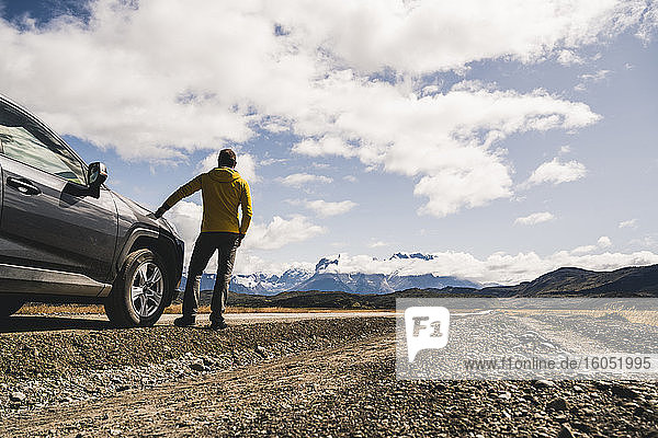 Mature man standing by car on dirt road at Torres Del Paine National Park  Patagonia  Chile