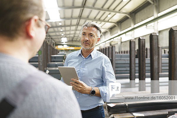 Businessman with tablet talking to employee in a factory