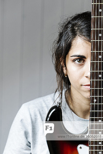 Junge Frau versteckt sich hinter einer E-Gitarre an der Wand zu Hause
