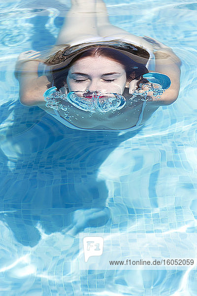 Nahaufnahme einer jungen Frau mit geschlossenen Augen beim Schwimmen im Pool eines Ferienortes