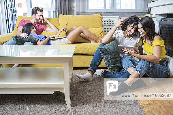 Glückliche junge Paare  die im Wohnzimmer sitzend Technologien nutzen