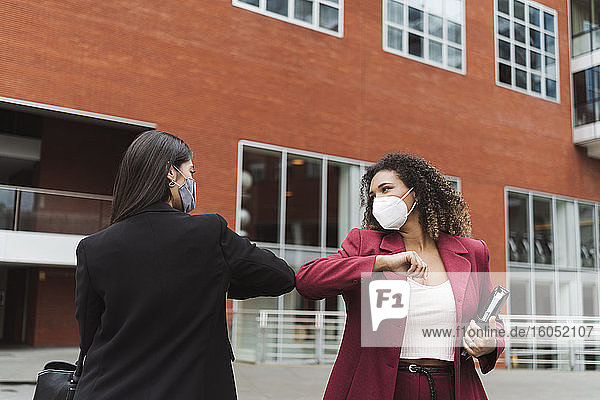Young multi-ethnic female professional giving elbow bump against building in city