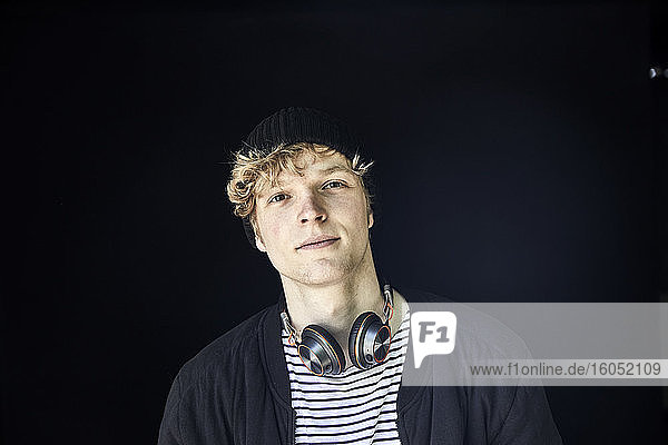 Porträt eines jungen Mannes mit Kopfhörern vor schwarzem Hintergrund