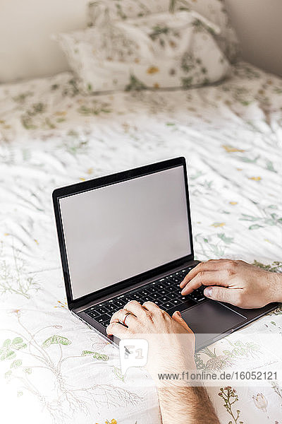 Mann mit Laptop auf dem Bett
