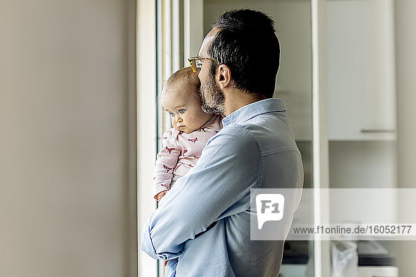 Father with baby looking out of the window at home
