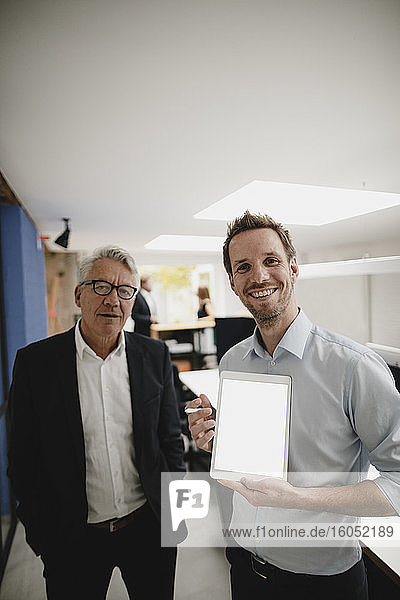 Zwei erfolgreiche Geschäftsleute stehen im Büro und benutzen ein digitales Tablet