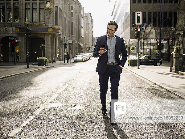 Mature businessman walking on a city street using smartphone