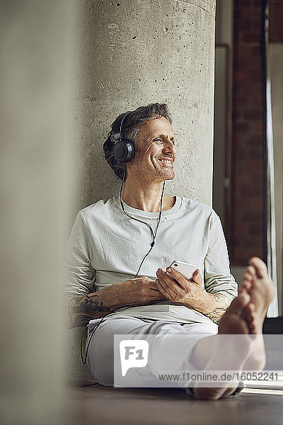 Lächelnder älterer Mann mit Kopfhörern  der in einer Loftwohnung Musik hört