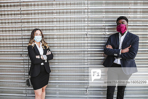 Geschäftsleute mit Masken und verschränkten Armen stehen an einer Wand in der Stadt