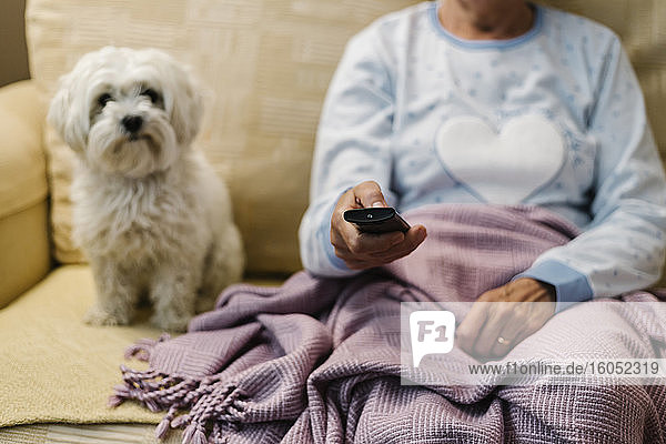 Kranke Frau im Ruhestand sitzt mit ihrem Hund auf dem Sofa und sieht zu Hause fern