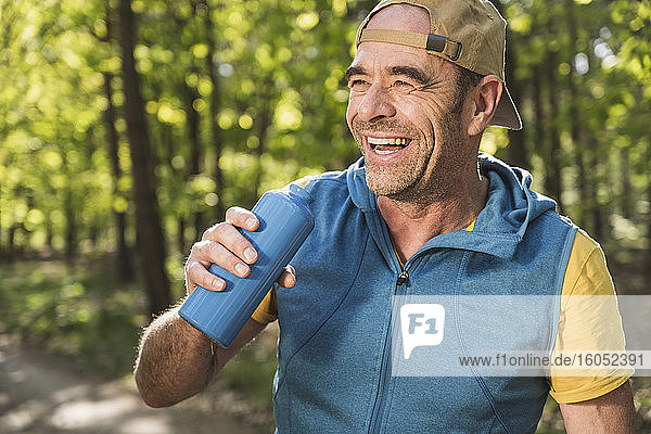 Happy man looking away while holding water bottle at park