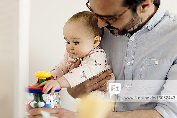 Father holding baby girl playing with toy