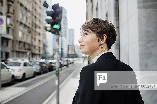 Smiling businesswoman looking away while standing against building in city