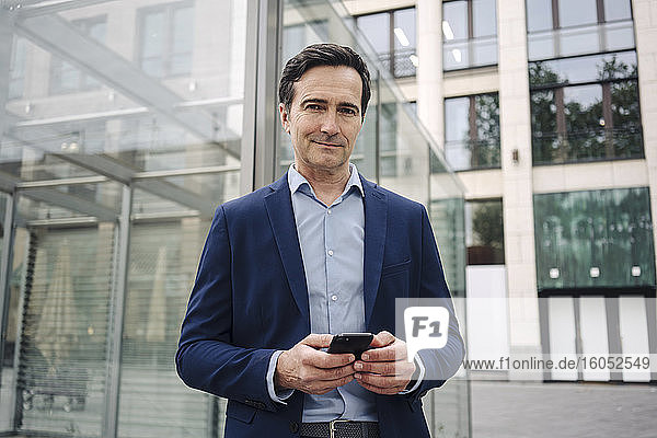 Portrait of a confident mature businessman with smartphone in the city
