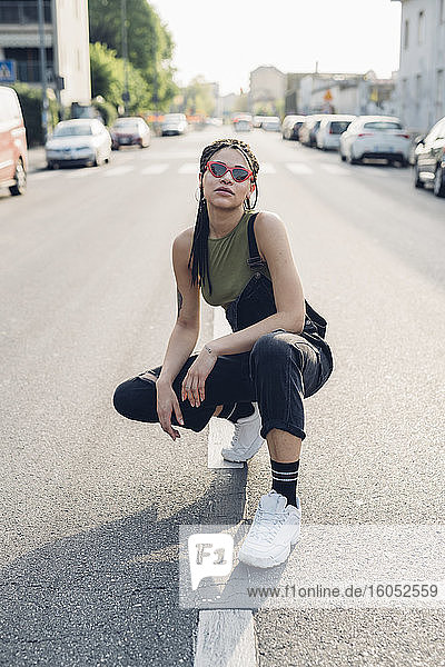 Portrait of a confident stylish young woman crouching on the street in the city