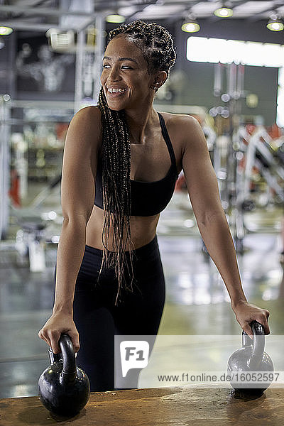 Lächelnde Sportlerin  die Kettlebells auf einer Holzkiste hält und wegschaut  im Fitnessstudio