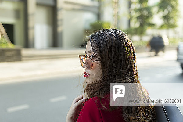 Nahaufnahme einer jungen Frau mit Sonnenbrille und Einkaufstasche auf einer Straße in der Stadt