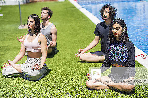 Junge multiethnische Freunde beim Meditieren und Yoga auf dem Rasen im Hinterhof bei sonnigem Wetter