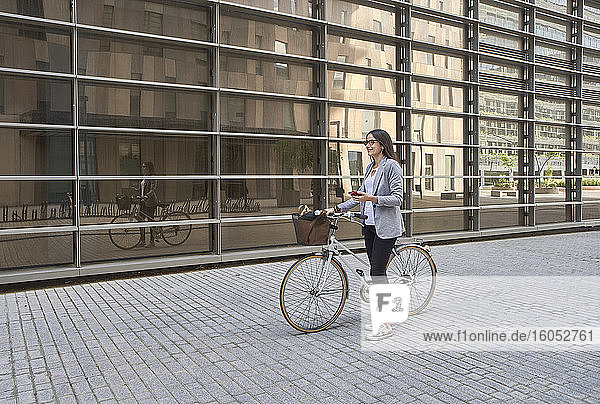 Nachdenkliche Geschäftsfrau steht mit Fahrrad auf der Straße in der Stadt