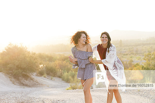 Cheerful female friends walking at countryside against clear sky