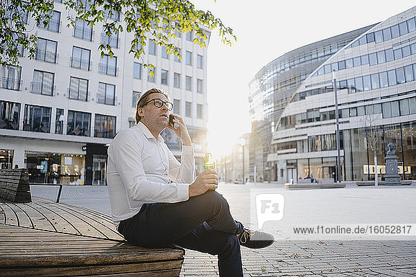Businessman sitting on a bench in the city at sunset talking on the phone
