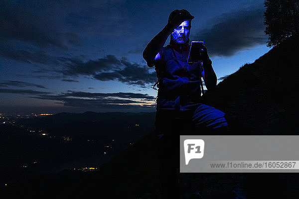 Man with headlamp checking map over smart phone on mountain at night  Orobie  Lecco  Italy