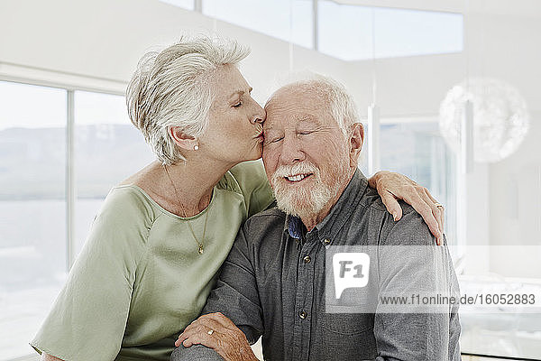 Ältere Frau küsst Ehemann in luxuriösem Strandhaus