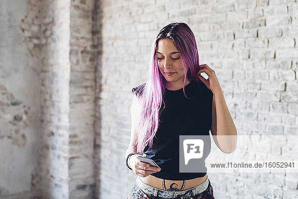 Stilvolle junge Frau mit rosa Haaren  die in einem Loft ihr Smartphone benutzt