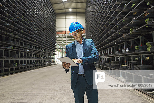 Mature businessman using tablet in a high rack warehouse of a factory