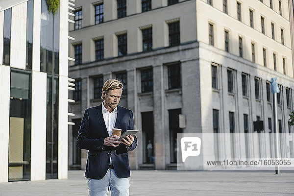 Businessman with takeaway coffee and tablet in the city
