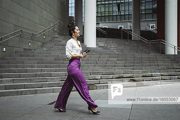 Modische junge Geschäftsfrau beim Spazierengehen mit Tagebuch in der Stadt