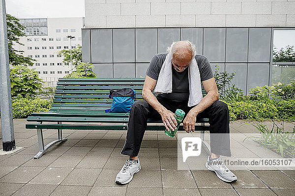 Müder älterer Mann mit Wasserflasche auf einer Bank in der Stadt