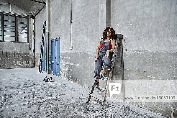 Female stonemason in overalls posing on wooden ladder at workshop