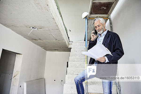 Architect on the phone holding building plan on a construction site