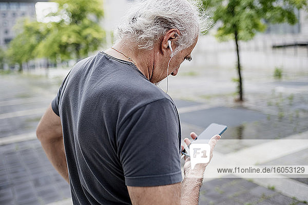 Nahaufnahme eines älteren Mannes  der ein Smartphone benutzt und Musik hört  während er im Freien steht