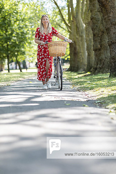 Happy woman walking with bicycle on footpath in public park during sunny day