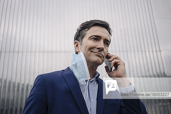 Mature businessman with protective face mask on the phone in the city