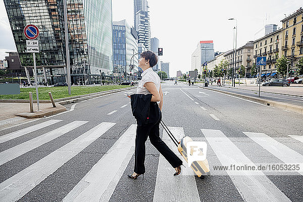 Female entrepreneur with suitcase crossing road in city