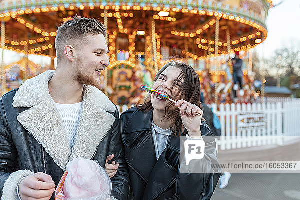 Glücklicher Mann  der seine Freundin ansieht  die im Vergnügungspark einen Lutscher isst