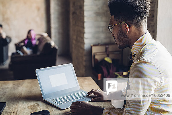 Kreativer Geschäftsmann mit Laptop im Loftbüro