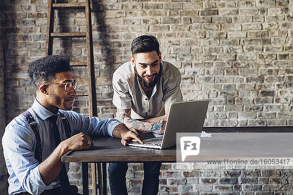 Two creative businessmen using laptop in loft office