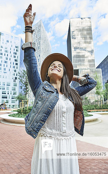 Happy woman standing with arms raised in city during sunny day