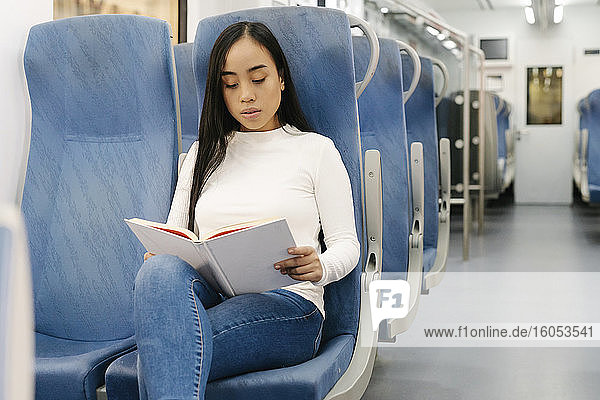 Young woman reading book while sitting on seat in train