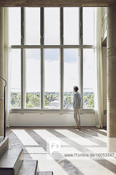Senior man looking out of window in a loft flat